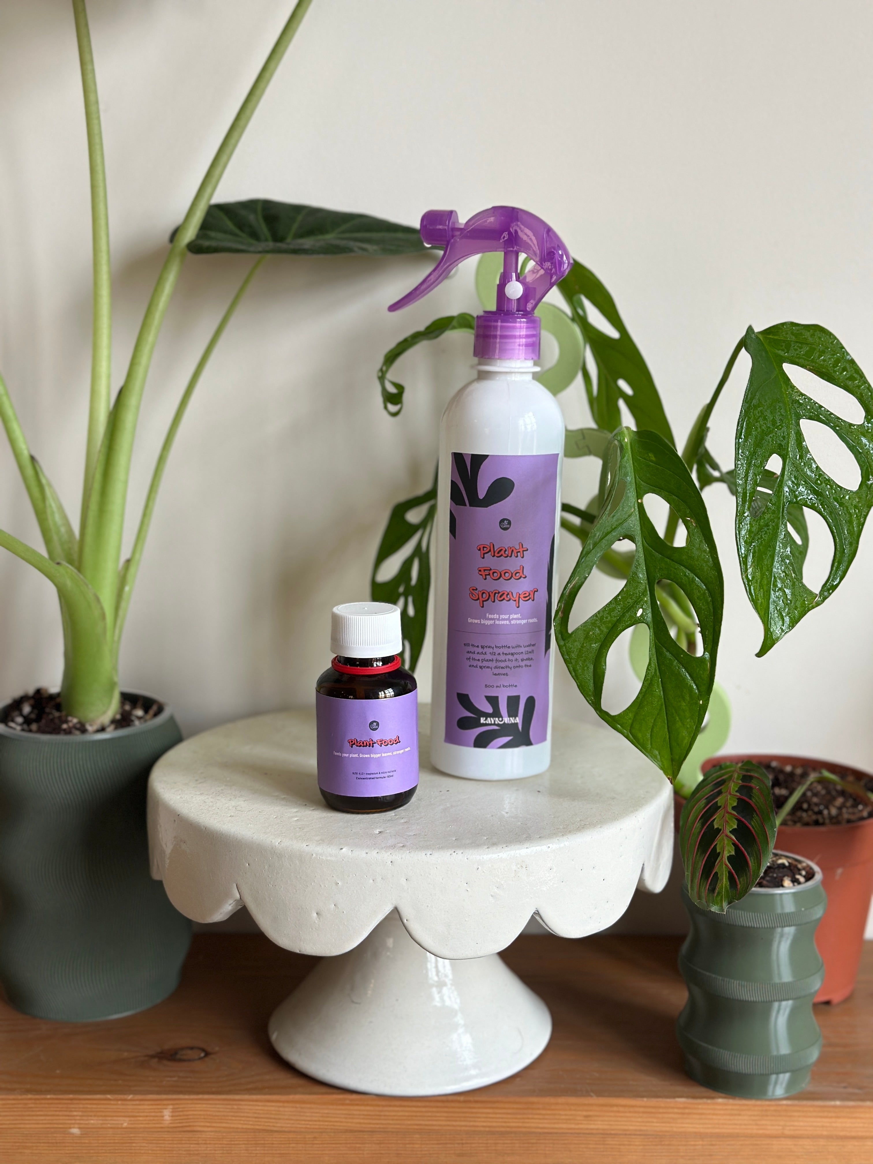 Two bottles of plant care products on a small white table with plants in the background.